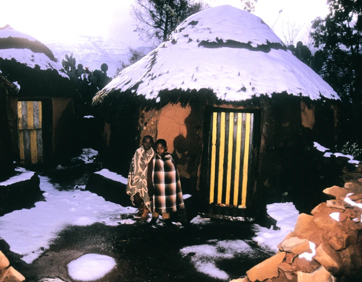 two woman standing in front of a small hut