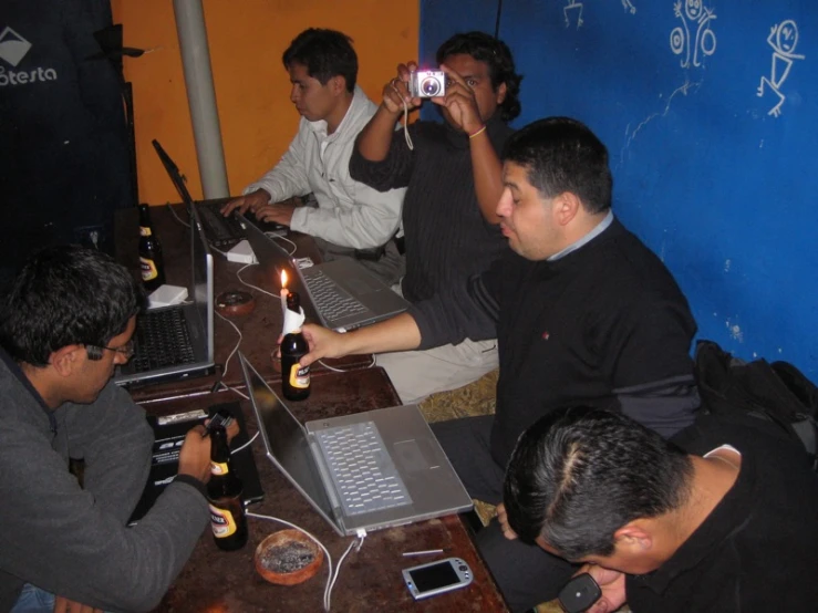 four people sit at a table in front of laptops and computers