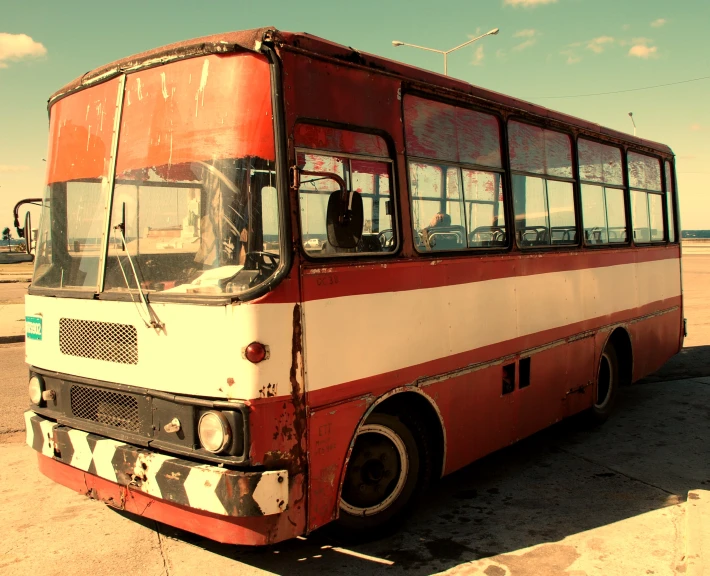an old red and white bus is in an empty lot