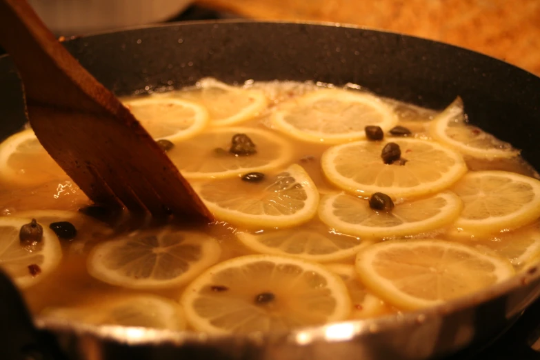 a frying pan filled with sliced lemons, garlic and broth
