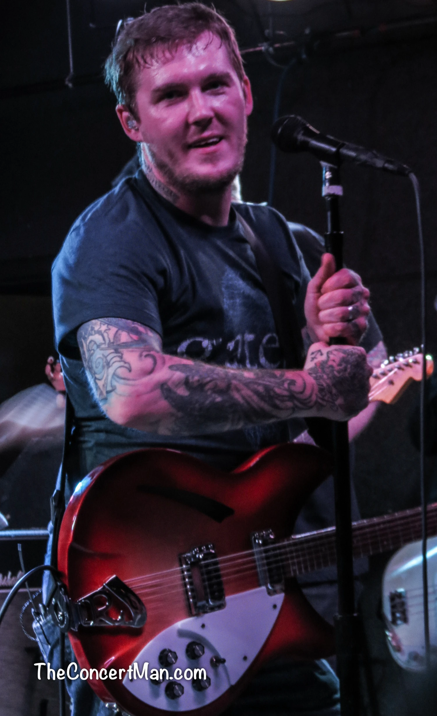 a tattooed man with his guitar at the microphone