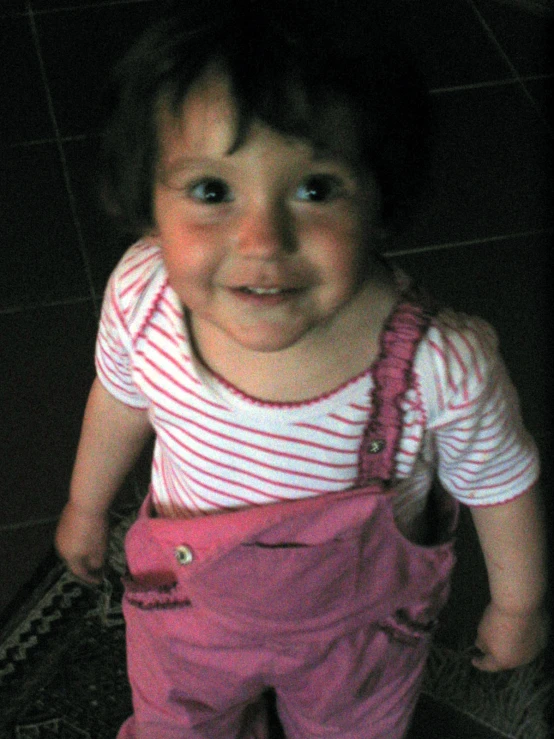 a toddler in pink overalls and white striped shirt