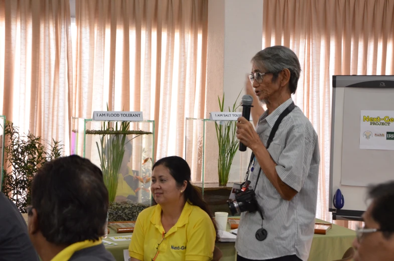 an older man speaking into microphone while standing next to two women