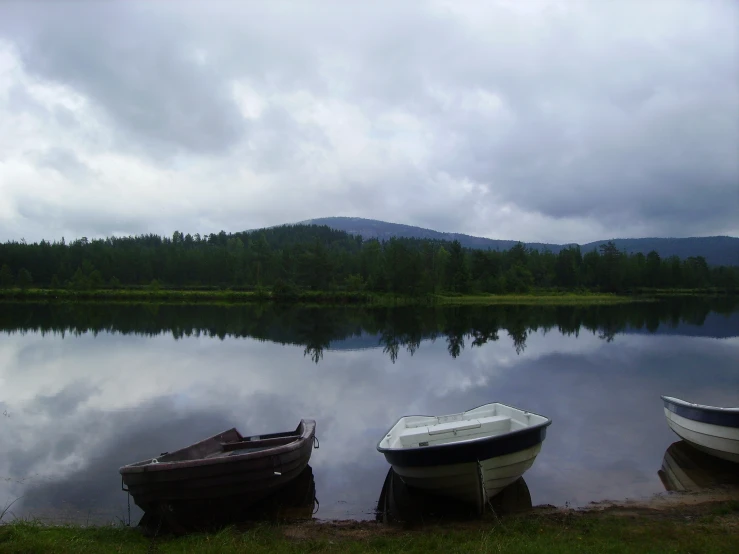 three boats sit in the water while a cloudy sky looms above