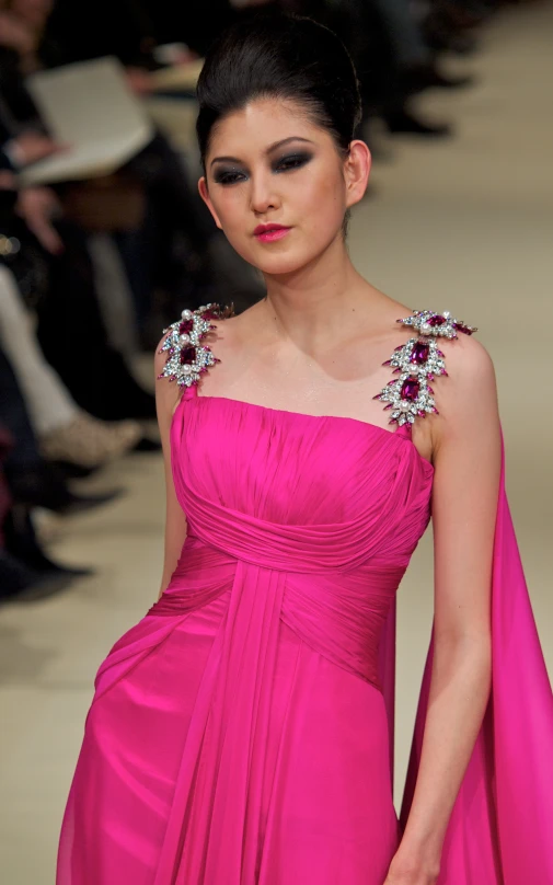 a lady walks down the runway in a pink gown