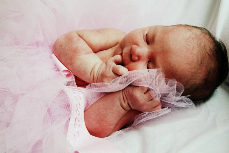 a newborn baby wearing a pink and white gown and posing for the camera