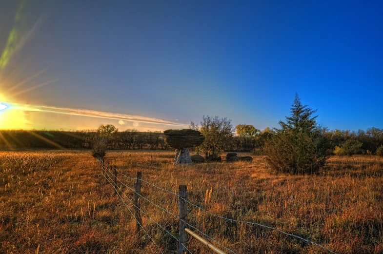 the sun rising over a field that has a barbed wire fence