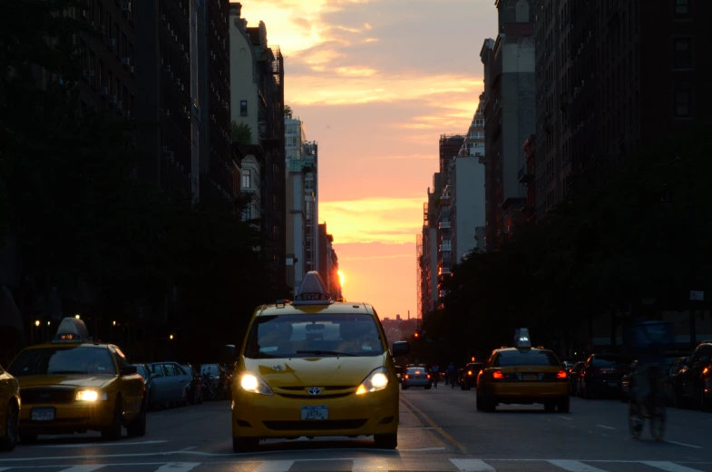 taxis and cabs driving down a street at sunset