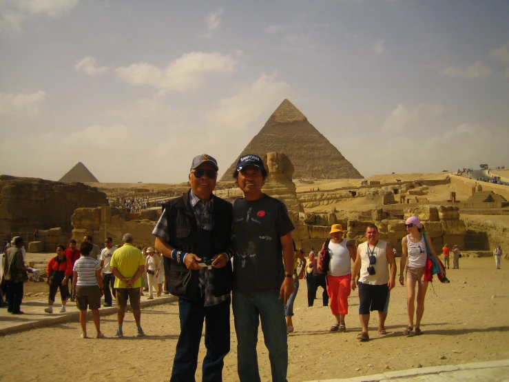 two men standing in front of the great pyramids with many other people