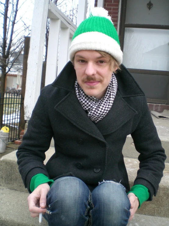 a guy in a hat sitting outside smoking