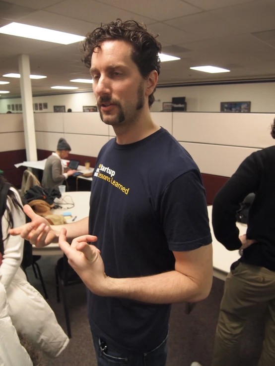 a young man standing in a office with his hands out and a third man standing next to him