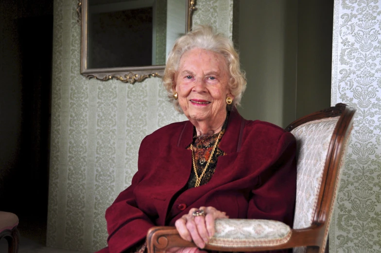 an older woman smiling for the camera while sitting in a chair