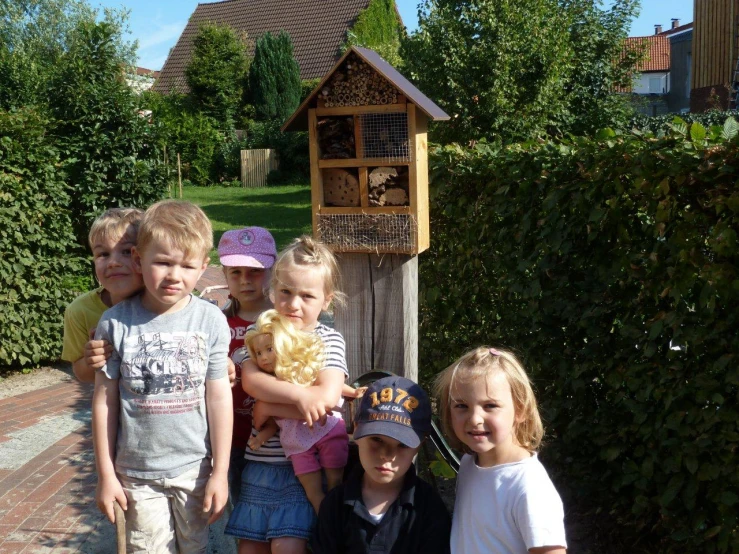 five children standing together in front of a small bird house