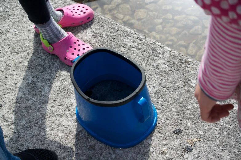 two girls are standing in pink clogs by the water