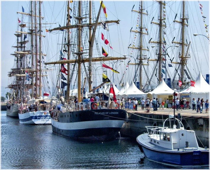 several large sailing ships docked near white tents