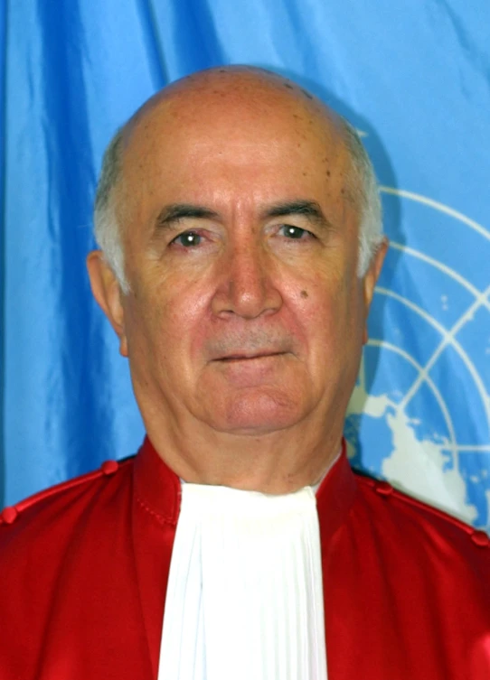 a man wearing a red jacket standing in front of a blue background