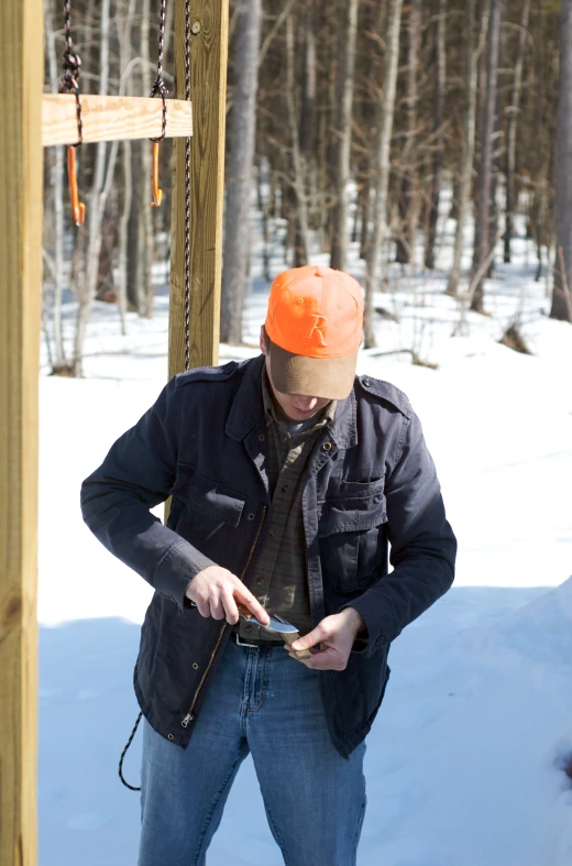 a man wearing an orange hat and a jacket using a cell phone