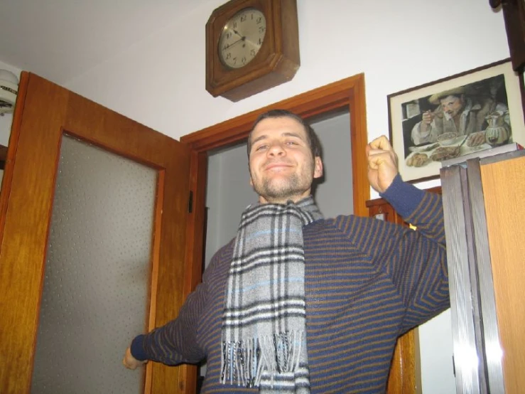 man wearing striped scarf pointing up in door way with clock above door