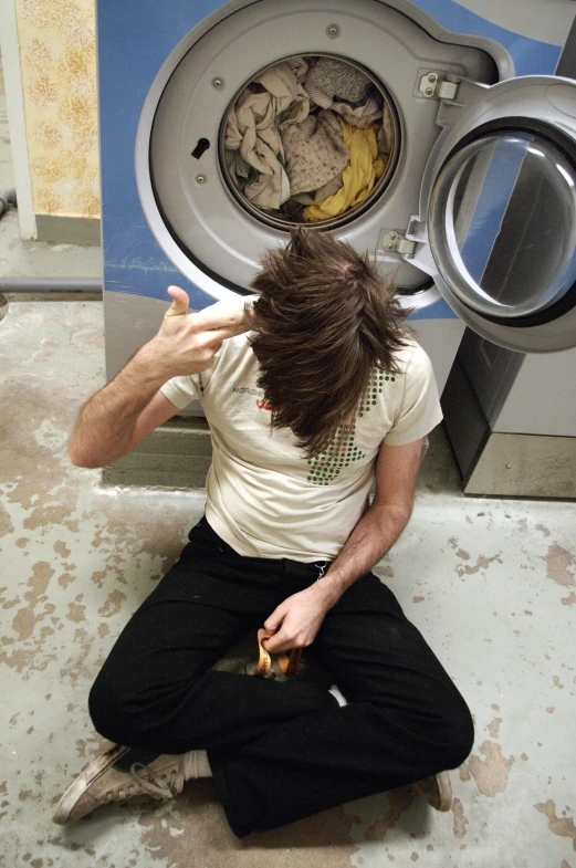 a man sitting on the floor in front of an open washing machine