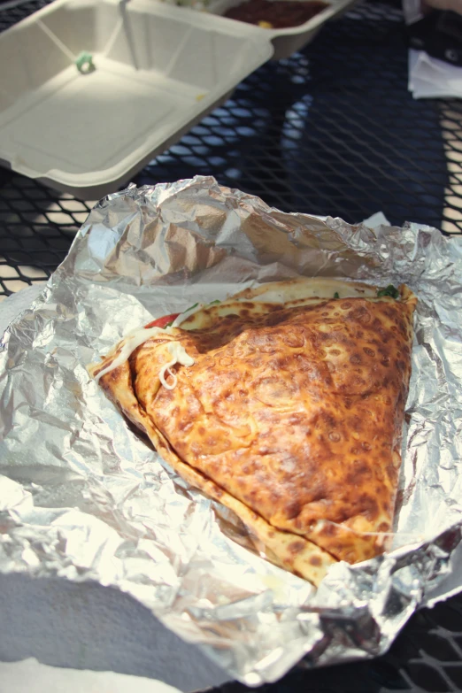 a slice of pizza on aluminum foil next to a serving dish