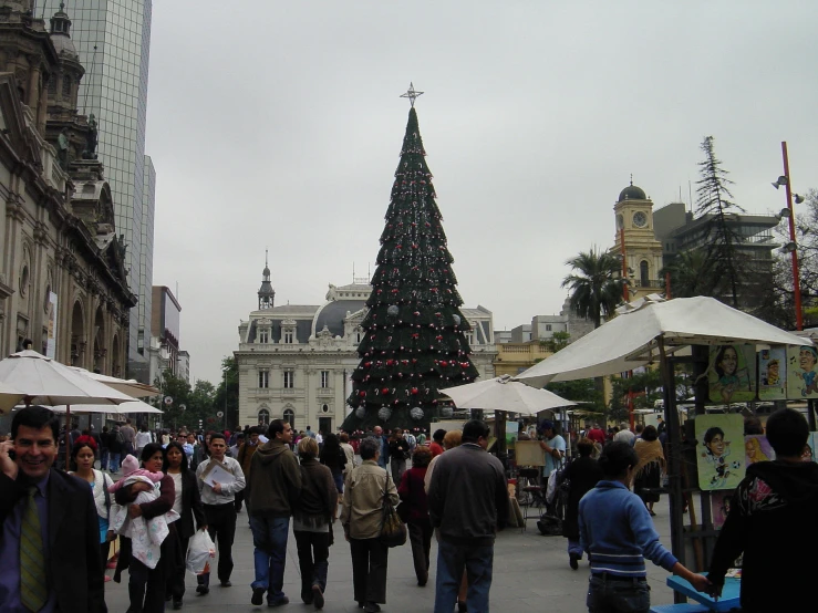 a group of people are walking around in front of a christmas tree