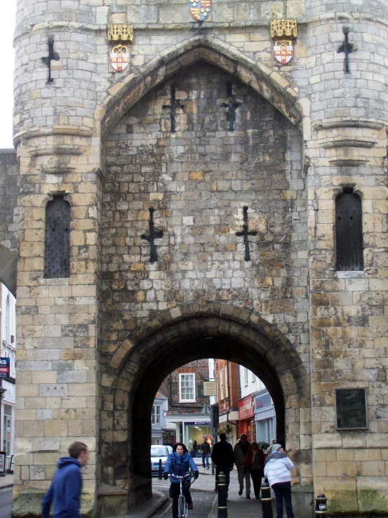 people are walking down a street near a stone castle gate