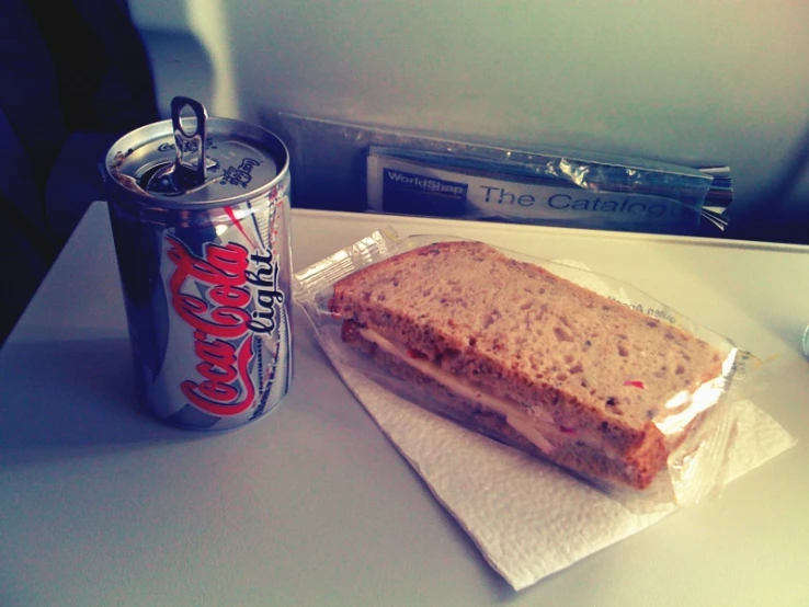 a can of soda and sandwich on an airplane tray