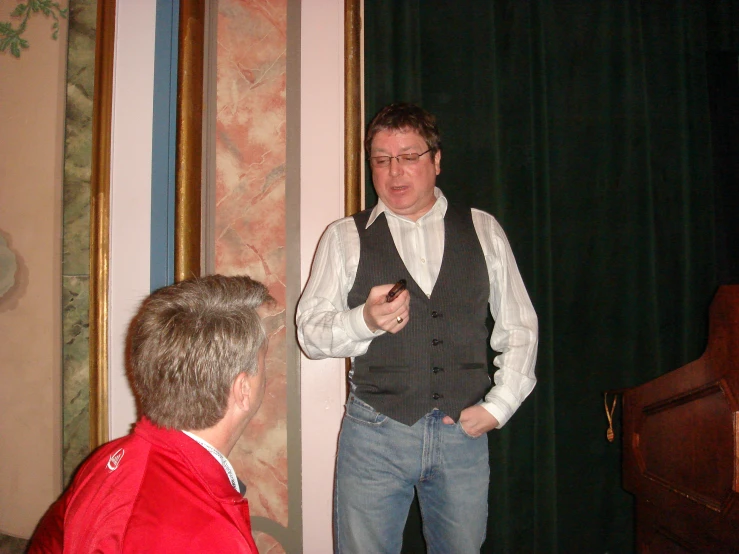 a man wearing a black vest standing in front of a speaker