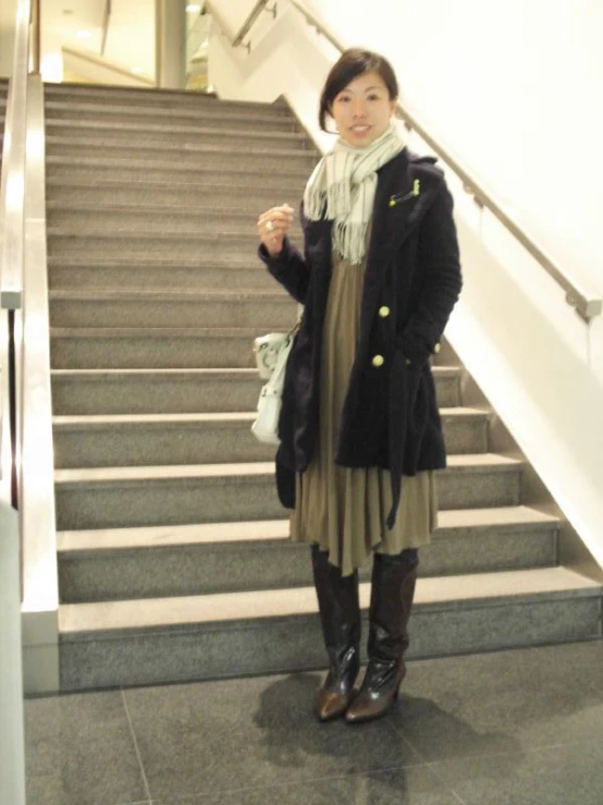 a woman wearing a long coat and boots posing in front of a banister with bags