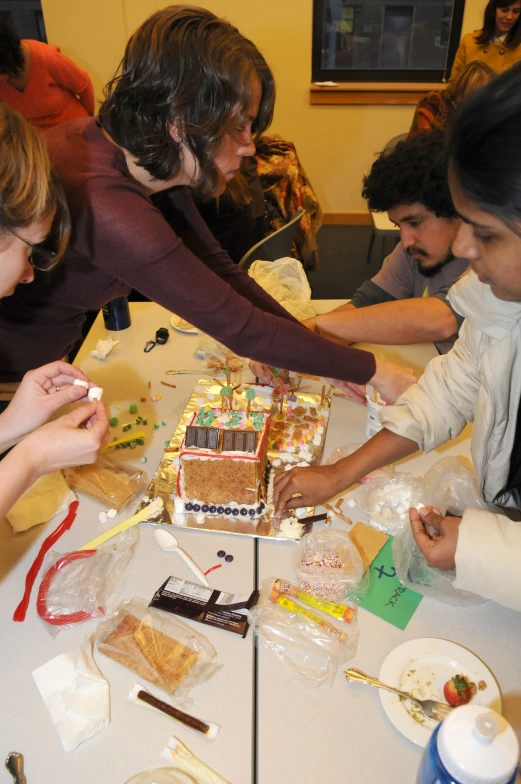 a group of young people gathered around a table  a gingerbread