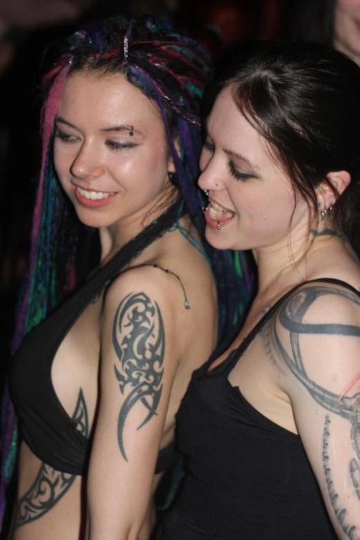 two females in black tank tops with tattoos on their arms