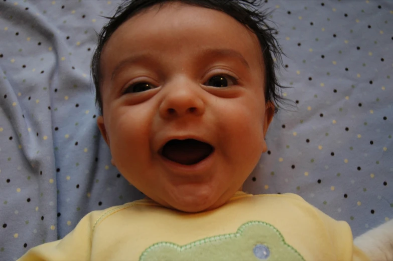 a smiling baby laying down on top of a bed