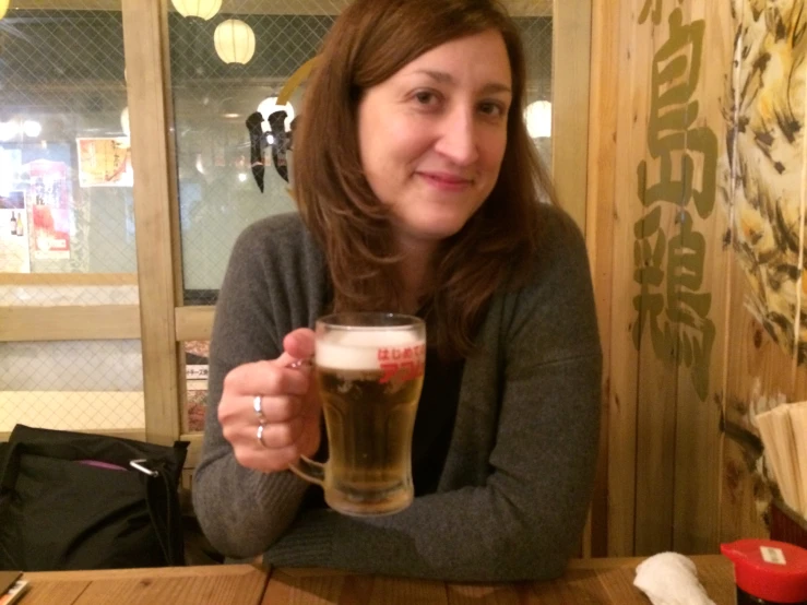 a woman sitting at a table holding up a beer