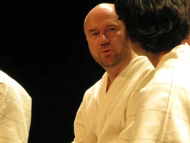 a bald man in white shirt talking to someone