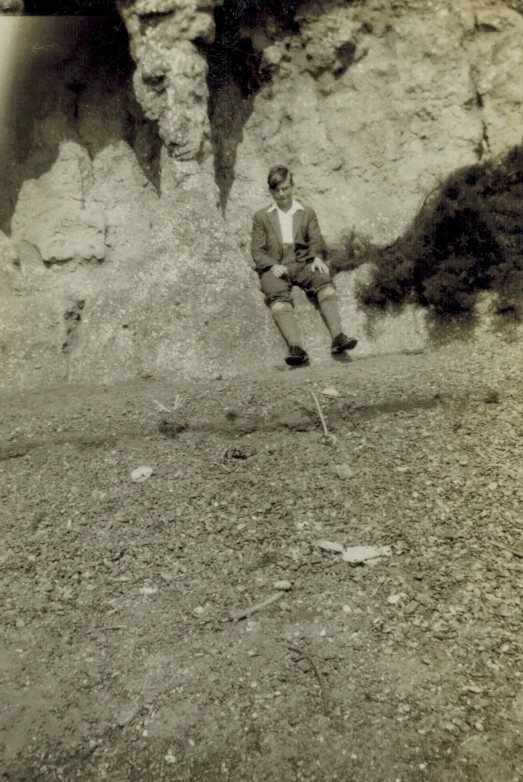 black and white pograph of man sitting on rock with rope