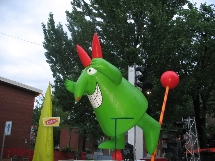 a green inflatable dragon character with a red hat on its head