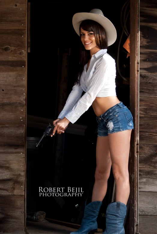 a beautiful woman in cowboy gear standing next to a wooden wall