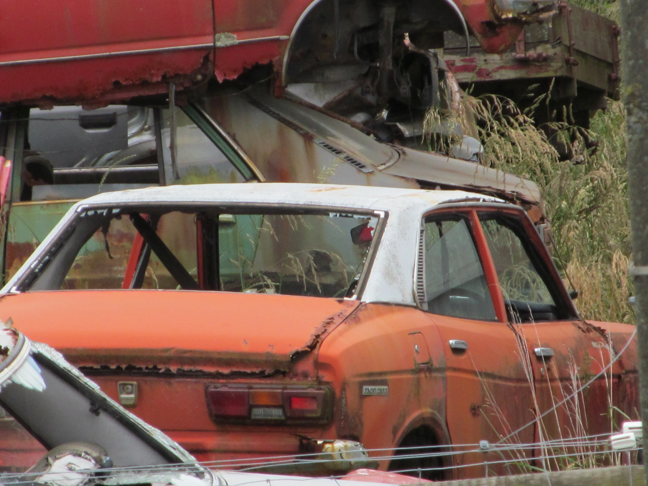 an old rusty car in front of some abandoned cars