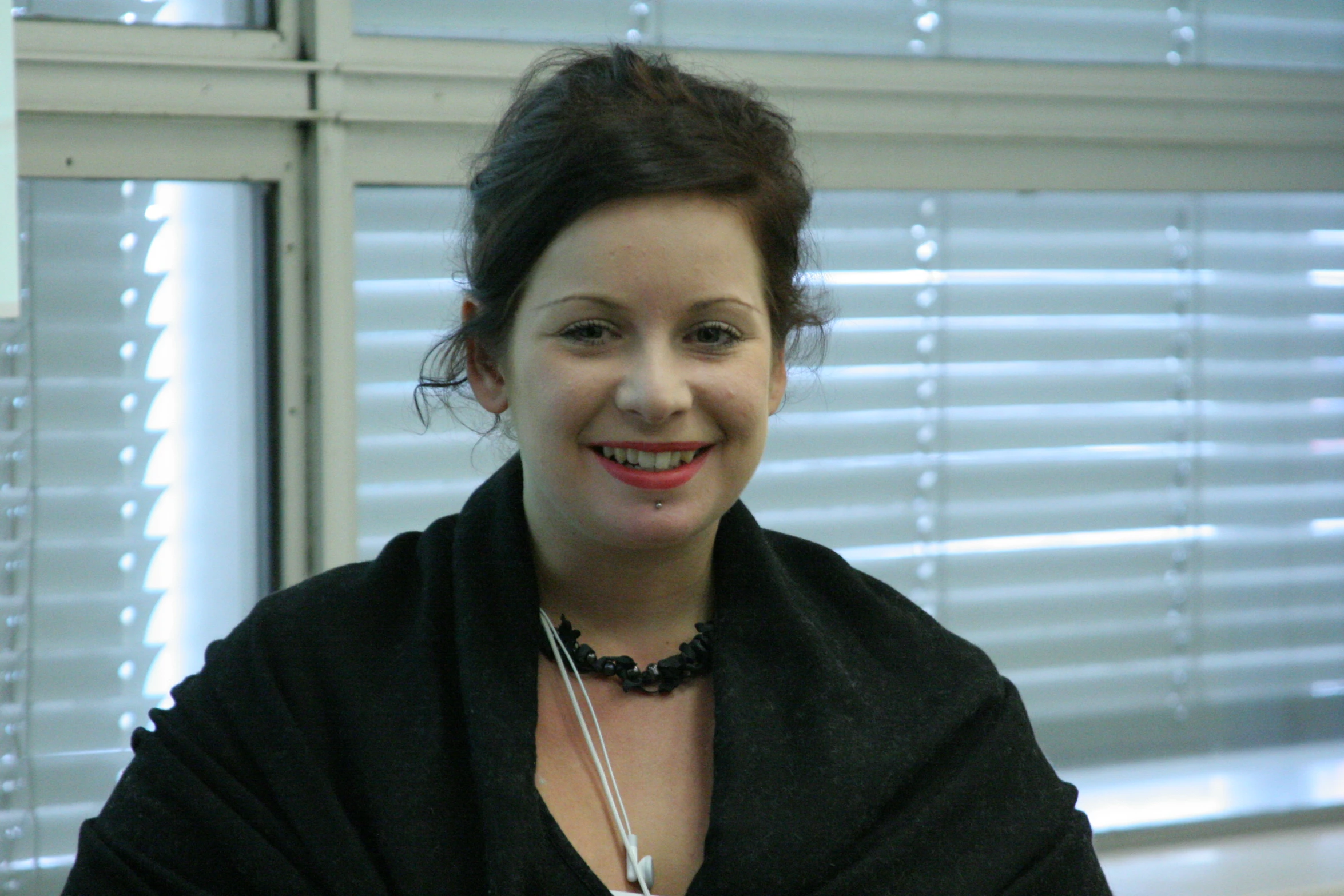 a woman posing in front of blinds with a black jacket on