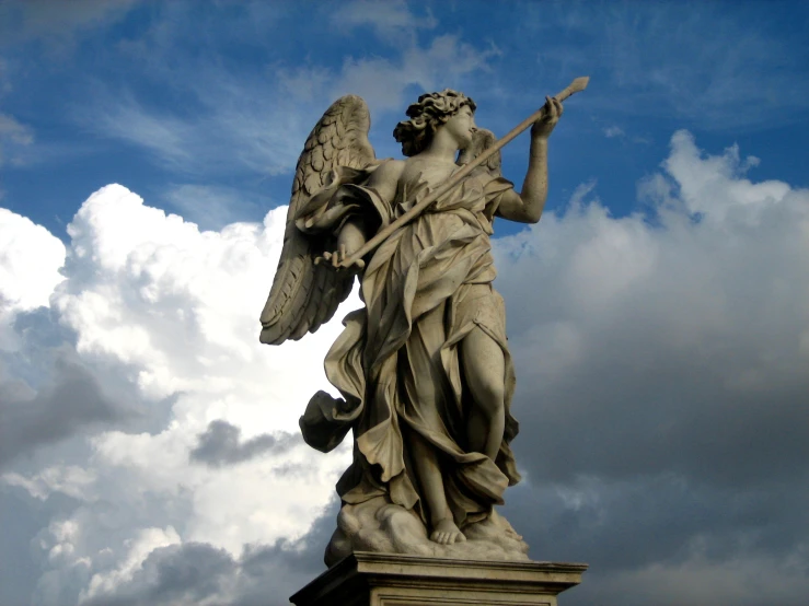 an angel statue holding a stick is standing on the sky