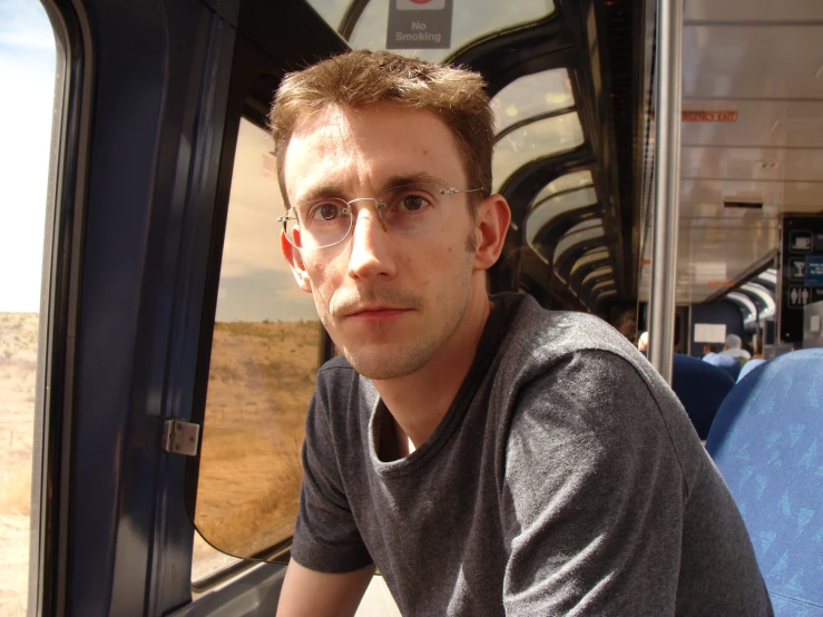 a man wearing glasses looking out of a train window