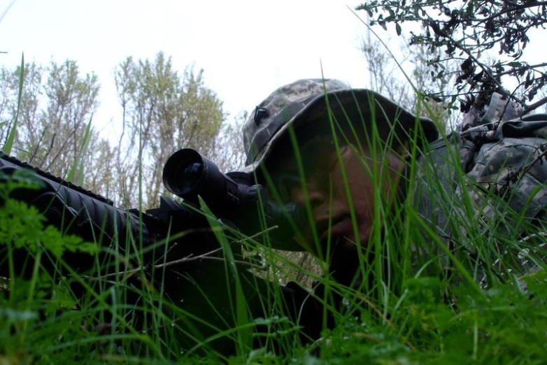 there is a man laying in the grass with rifle in hand