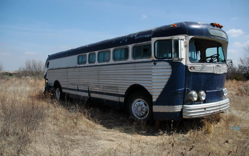 an older school bus sits empty in the middle of a dry grass plain