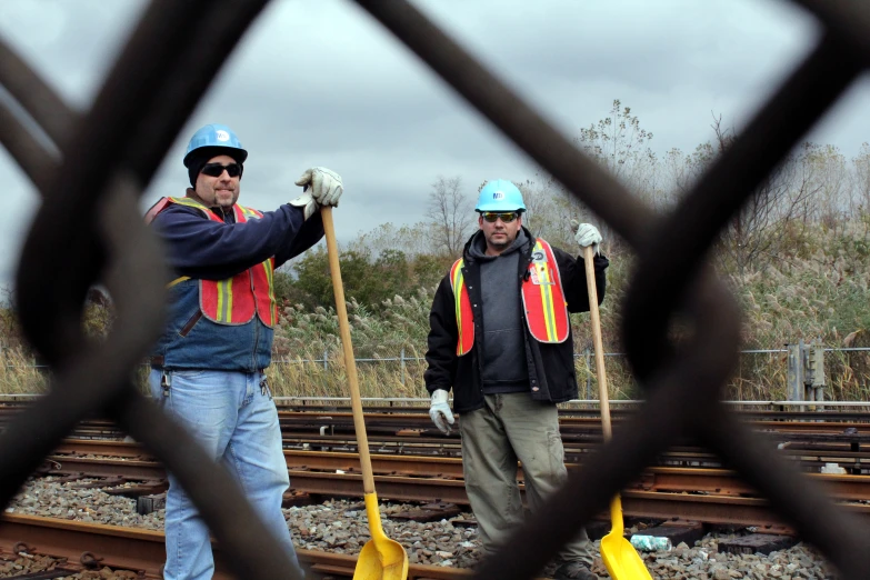 two people standing on train tracks with shovels