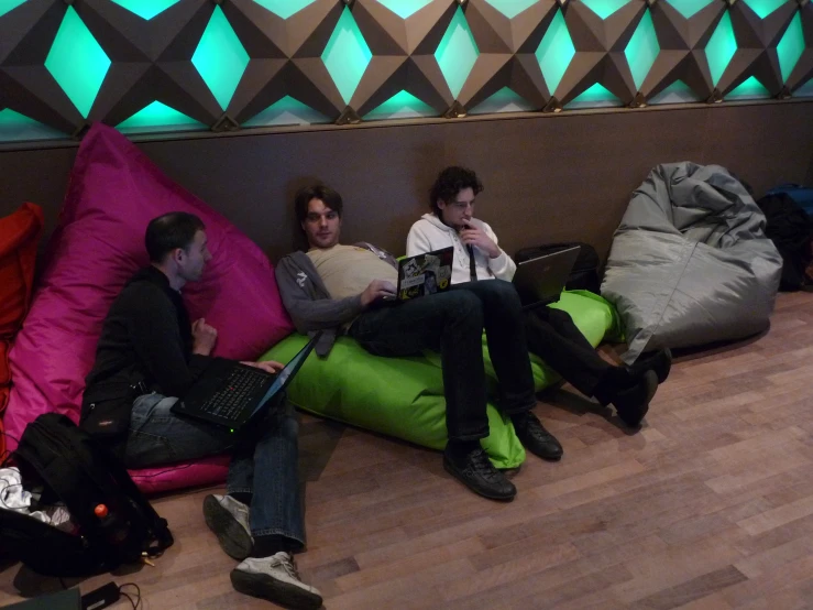 three people sitting on beanbag pillows using laptops