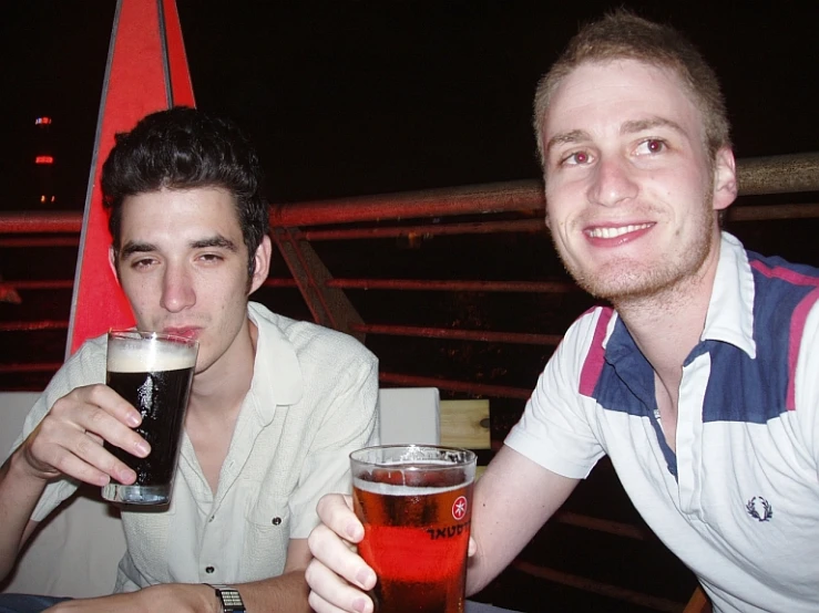 two men sitting at an outdoor table drinking beer