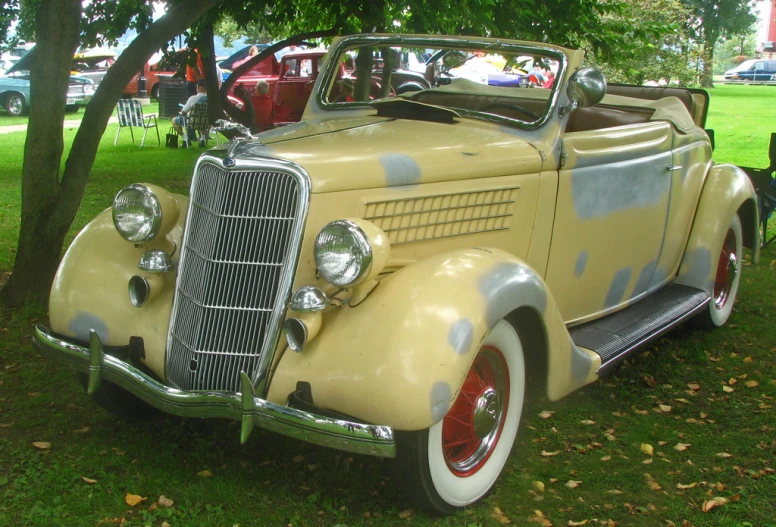 an old yellow car sitting on top of a lush green field