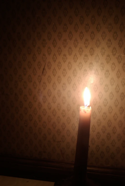 a lit candle in front of a wallpapered background