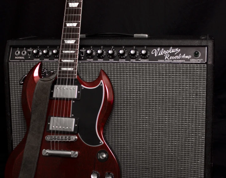 red guitar with amp standing against dark background