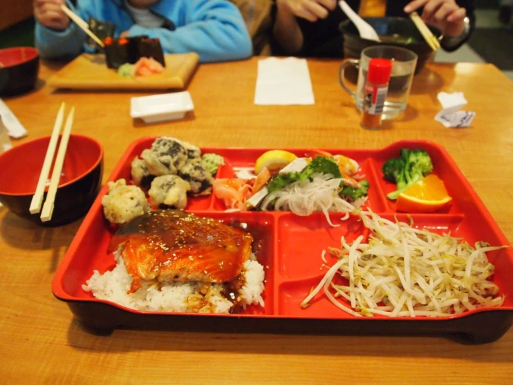 a long, red plastic plate on top of a table covered in rice and meat